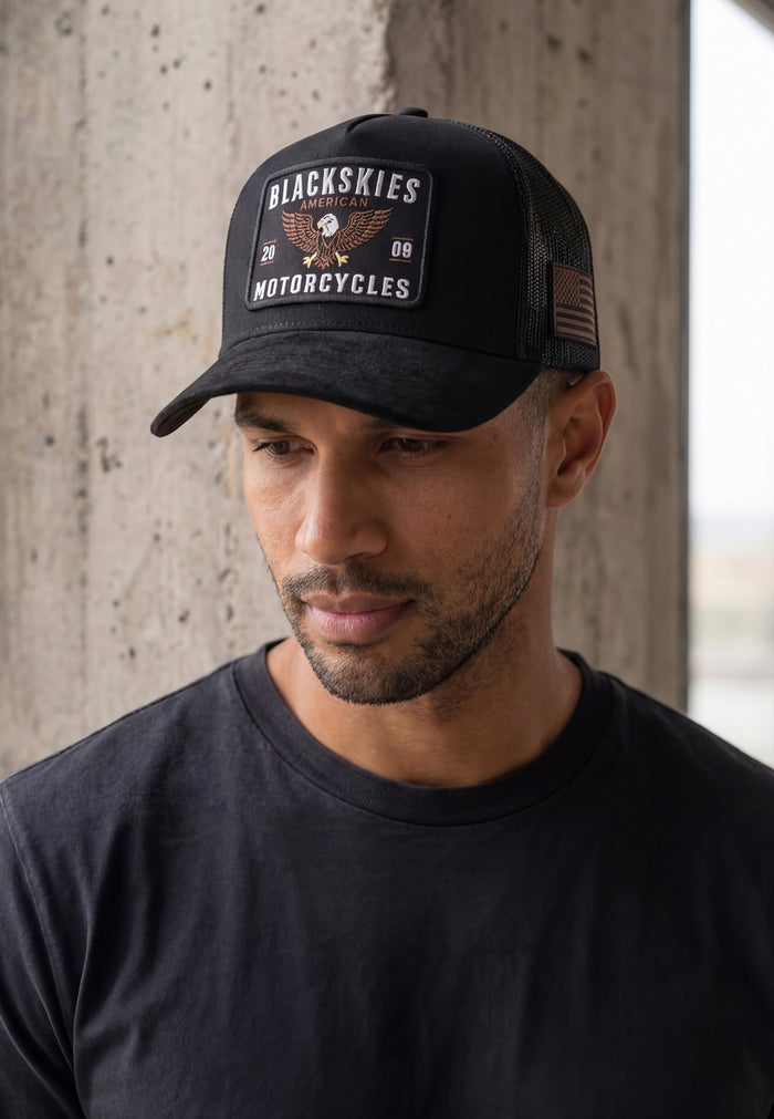 Man wearing a black cap with 'Blackskies Motorcycles' logo against a concrete wall.