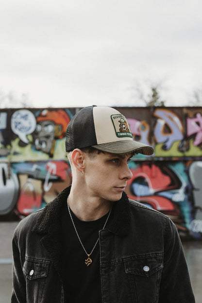 Person wearing a cap with a logo in front of a graffiti-covered wall