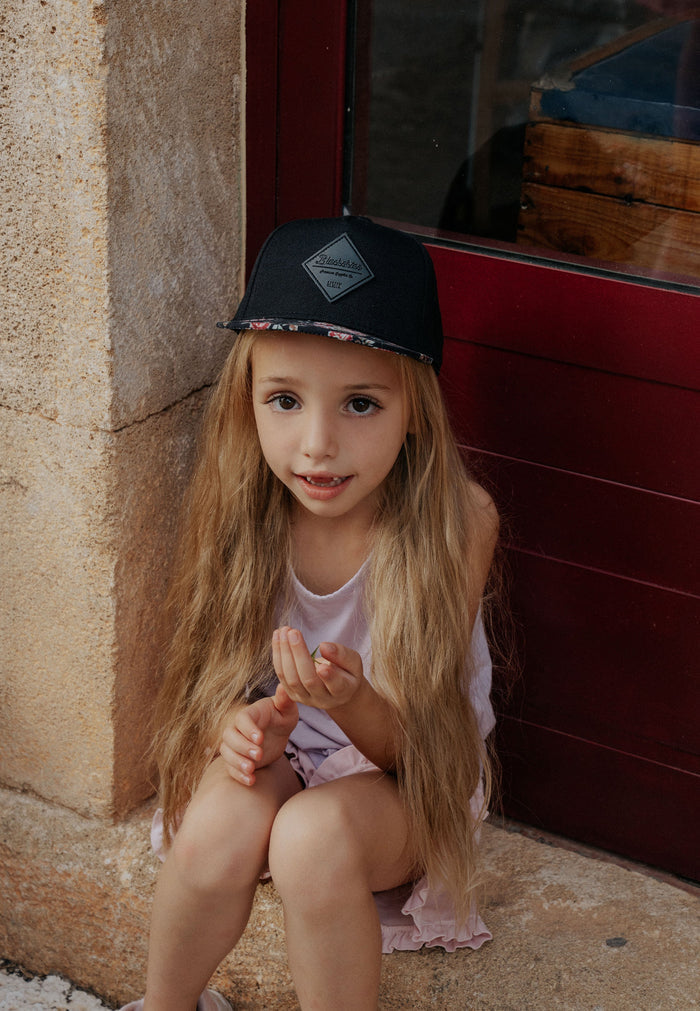 Young girl with a black cap sitting against a textured wall.