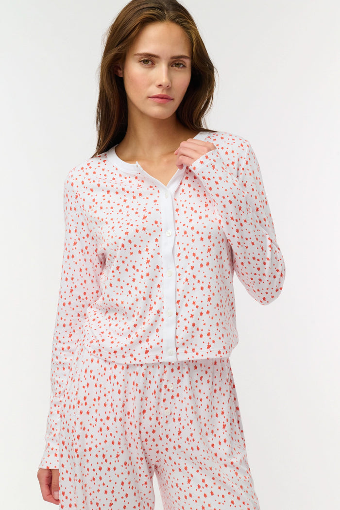 A woman wears the Roller Rabbit Étoiles Nessa Cardigan over a long-sleeve white pajama set with red polka dots, made from cozy Pima cotton in Peru, standing against a light background and looking at the camera with a relaxed expression.