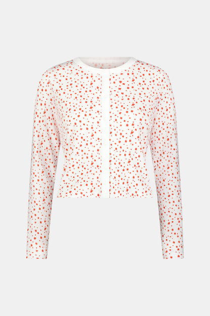 A woman wears the Roller Rabbit Étoiles Nessa Cardigan over a long-sleeve white pajama set with red polka dots, made from cozy Pima cotton in Peru, standing against a light background and looking at the camera with a relaxed expression.