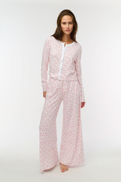 A woman wears the Roller Rabbit Étoiles Nessa Cardigan over a long-sleeve white pajama set with red polka dots, made from cozy Pima cotton in Peru, standing against a light background and looking at the camera with a relaxed expression.