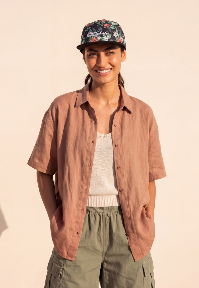 Person wearing a brown shirt, floral cap, and green pants on a beige background