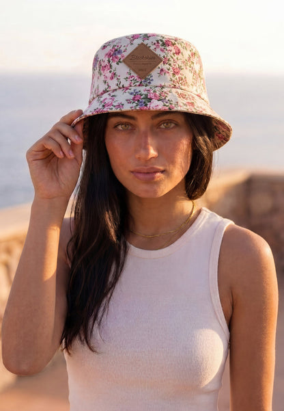 Woman wearing a floral bucket hat from blackskies in a holiday sun setting
