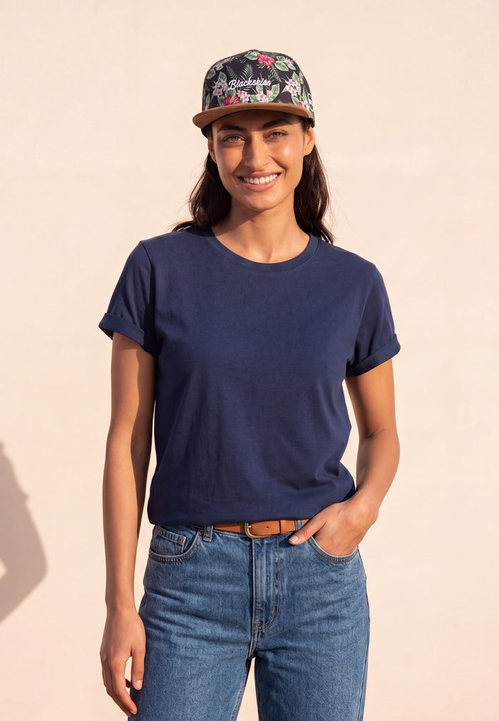 Woman wearing a navy t-shirt, floral cap, and blue jeans on a beige background