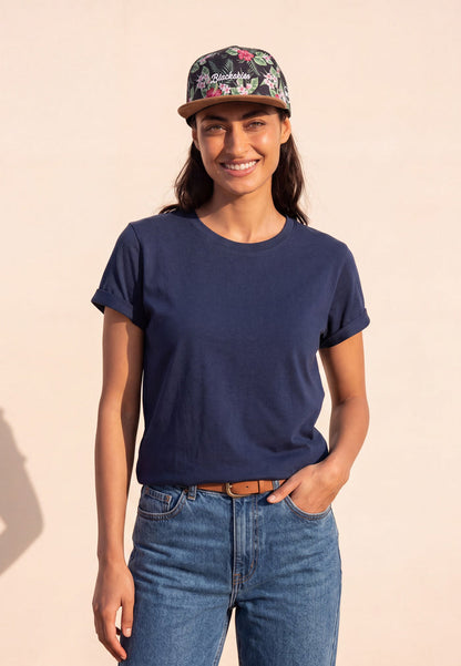 Woman wearing a navy t-shirt, floral cap, and blue jeans on a beige background
