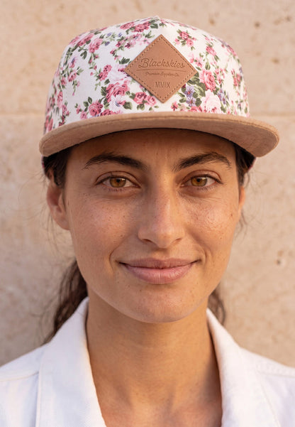 Woman wearing a white floral cap with a visible blackskies brand logo against a neutral background