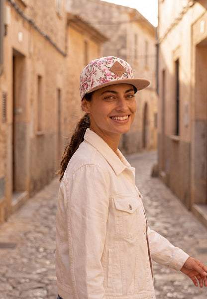 Woman wearing a floral cap and light jacket walking down a sunlit street.