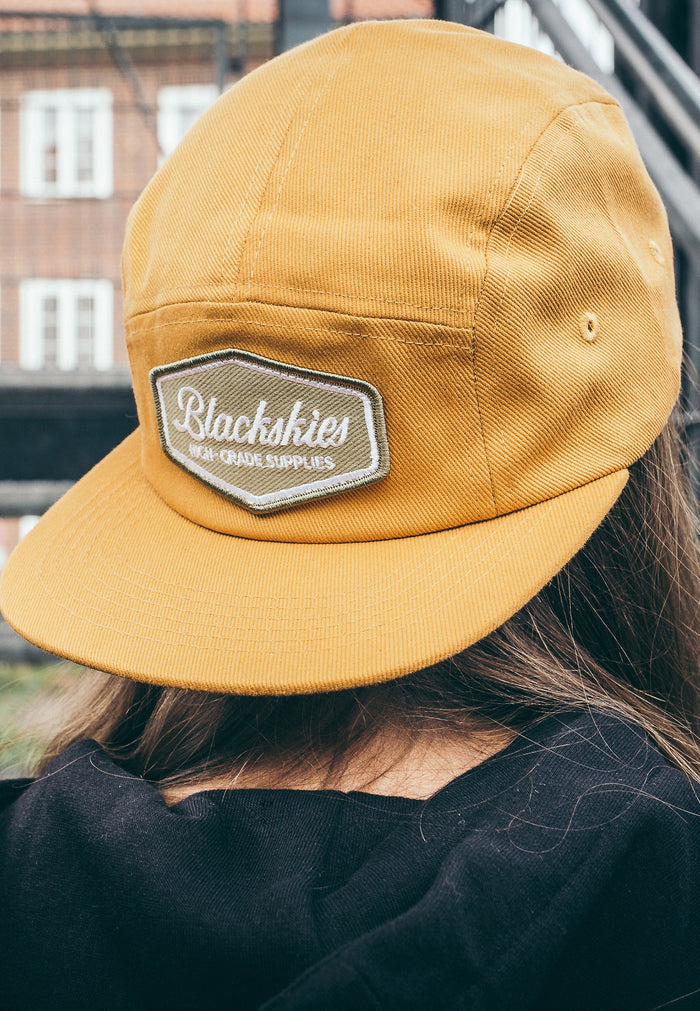 Yellow cap with a brand logo worn by a person, blurred background