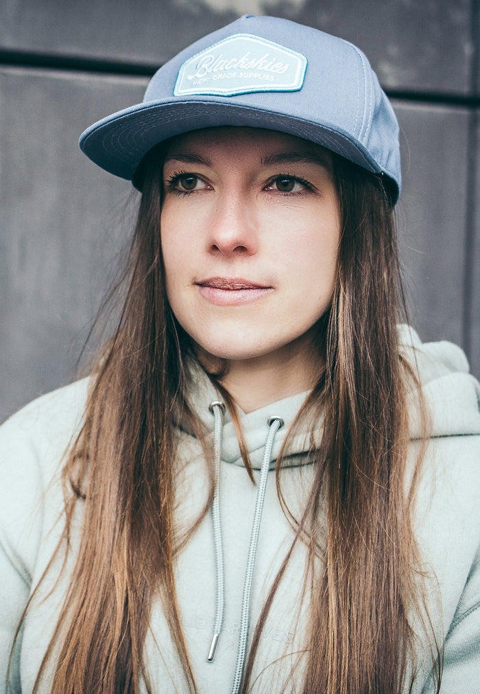 Woman wearing a gray cap and hoodie against a gray background