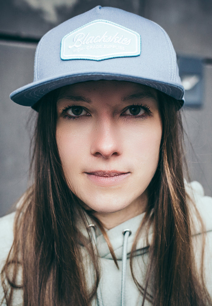 Person wearing a gray cap with a logo, looking directly at the camera.