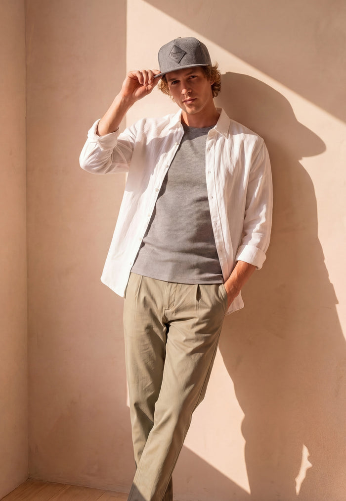 Man wearing a white shirt, gray sweater, and beige pants against a beige wall.