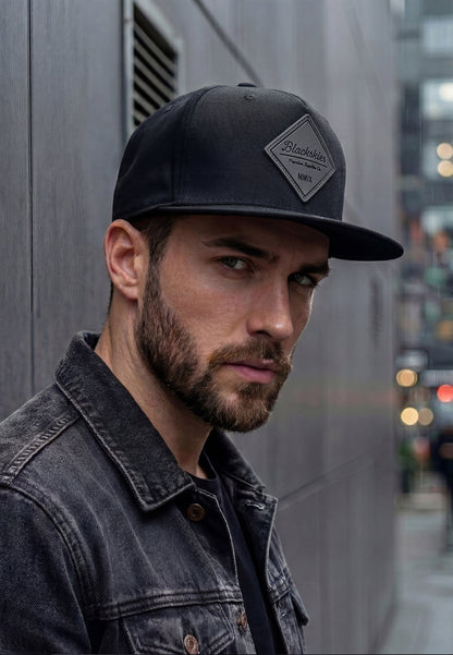 Man wearing a black cap and denim jacket against an urban background