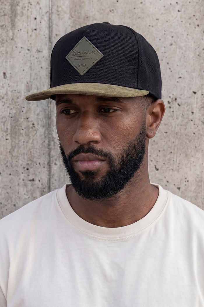 Man wearing a black cap with a beige bill against a concrete wall
