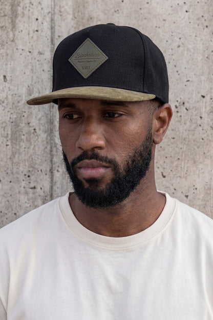 Man wearing a black cap with a beige bill against a concrete wall
