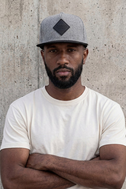 Man wearing a gray cap and white t-shirt against a concrete wall