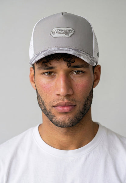 Man wearing a gray cap with a brand logo on a plain background