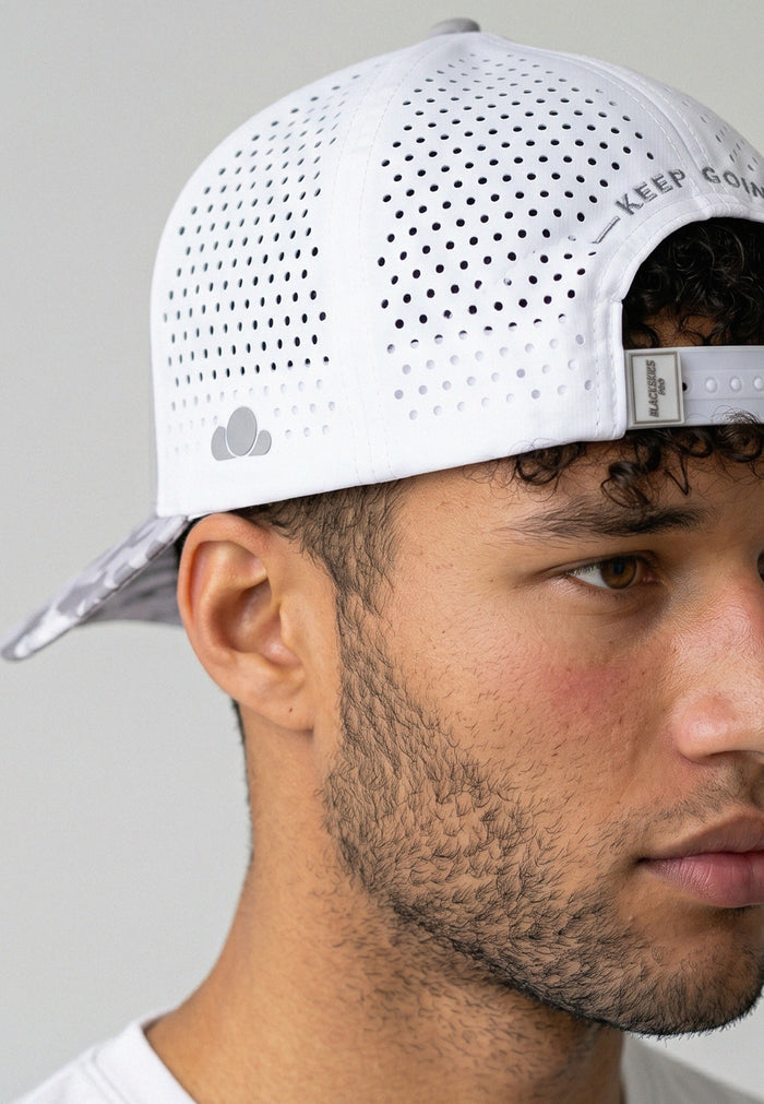 Person wearing a white perforated cap with a brand logo on a gray background