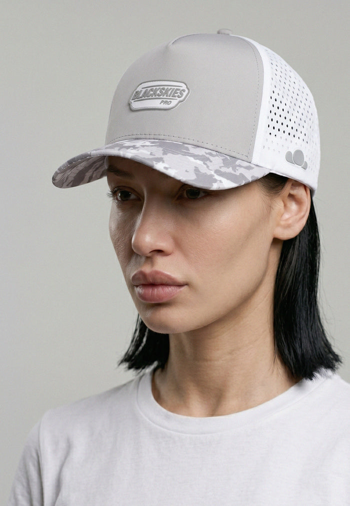 Person wearing a gray and white cap with a visible brand logo on a plain background