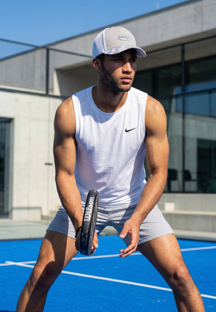 Man playing paddle tennis on a blue court wearing a white tank top and shorts.