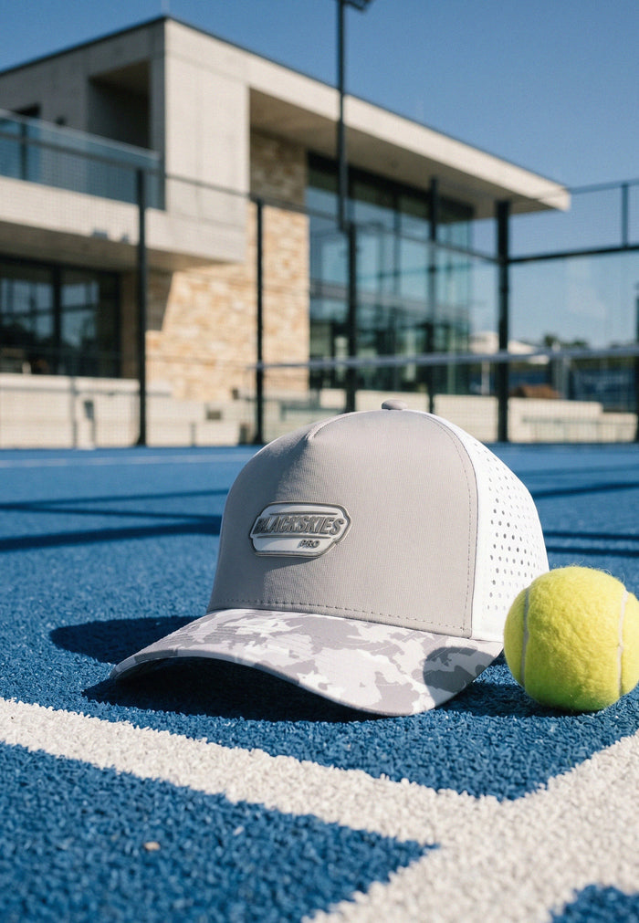 Gray cap with white mesh and a logo on a tennis court, with a tennis ball nearby.