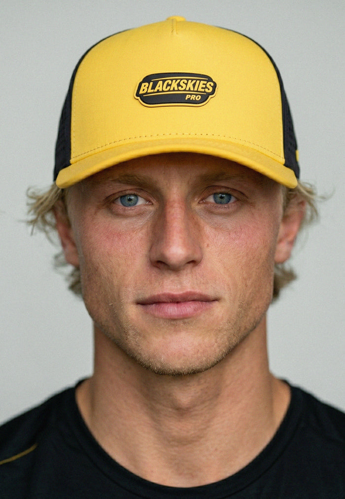 Man wearing a yellow and black cap with 'Blackskies Pro' logo against a plain background