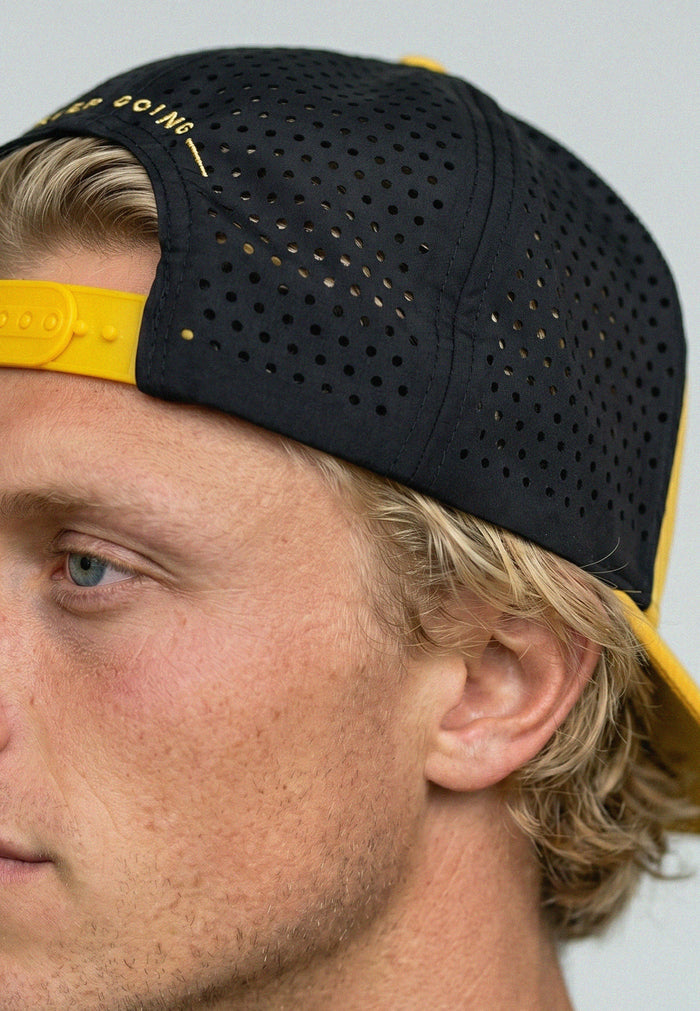 Person wearing a black and yellow cap with visible branding on a neutral background