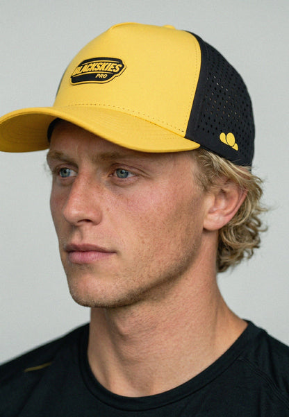 Person wearing a yellow and black cap with a visible brand logo on a plain background