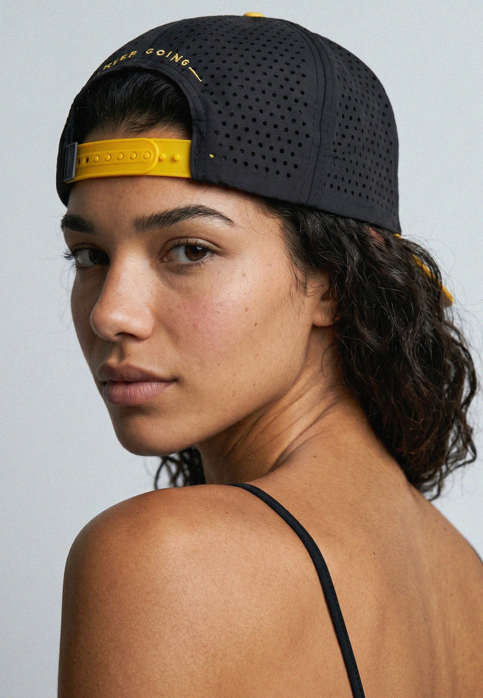 Woman wearing a black cap with yellow interior against a gray background