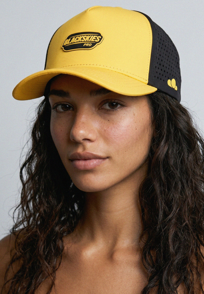 Woman wearing a yellow and black cap with 'Blackskies Pro' logo on a gray background