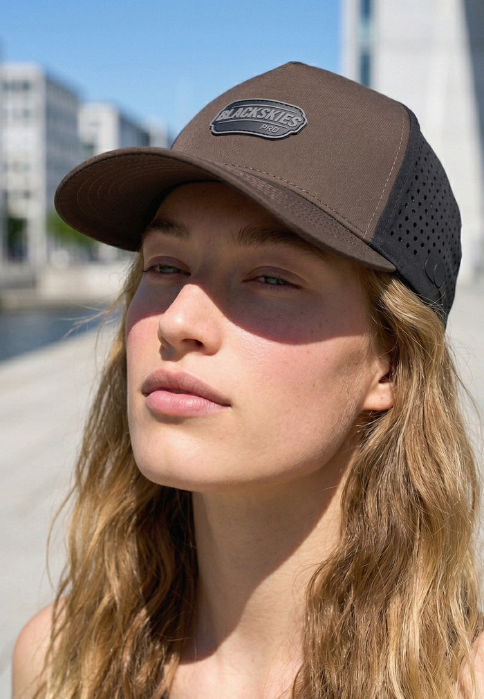 Woman wearing a brown and black cap with 'Blackskies' logo outdoors.
