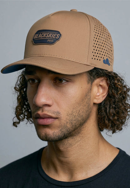 Man wearing a tan cap with a visible brand logo against a gray background