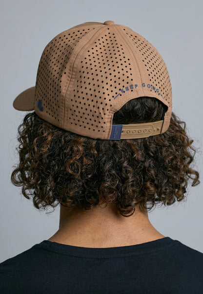 Person wearing a beige cap with a brand logo on a gray background