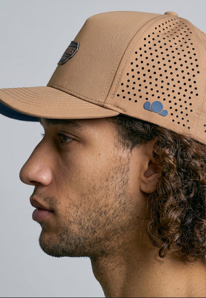 Man wearing a tan baseball cap with a perforated design on a gray background