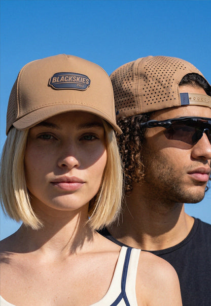 Two people wearing tan caps with 'Blackskies' logo against a clear blue sky.