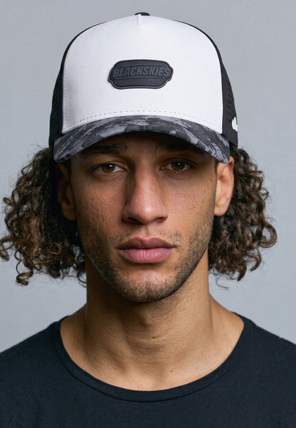 Man wearing a black and white cap with a brand logo on a gray background