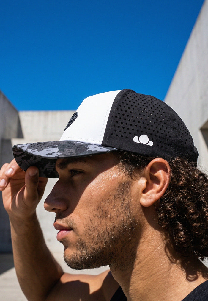 Man wearing a black and white cap with a logo against a blue sky.