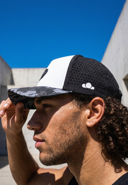 Man wearing a black and white cap with a logo against a blue sky.