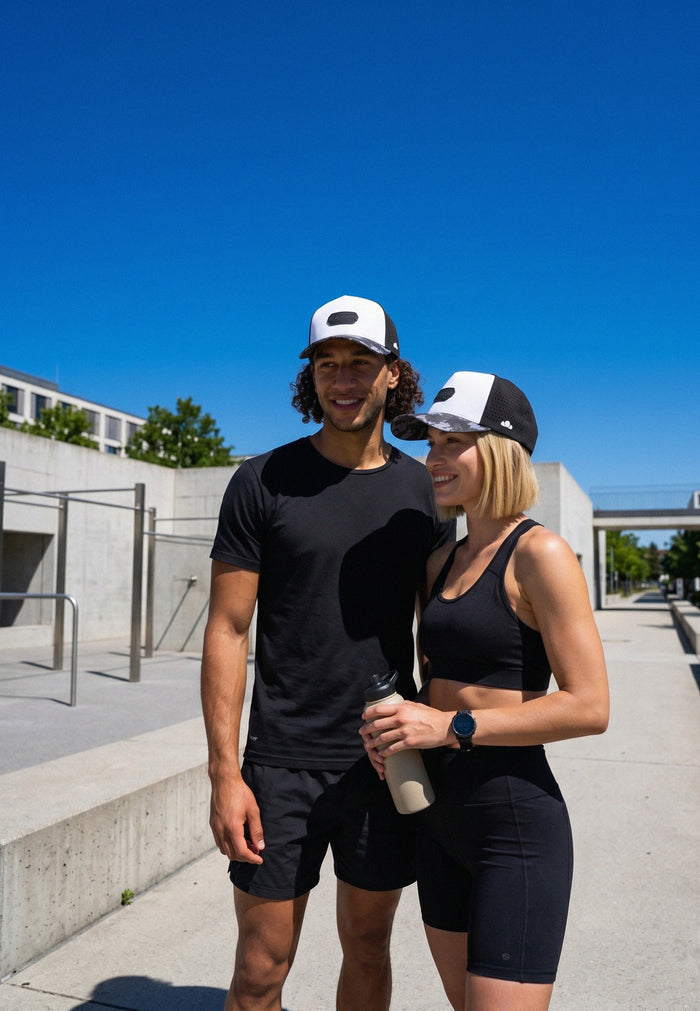Two people wearing black athletic wear with white hats standing outdoors on a sunny day.