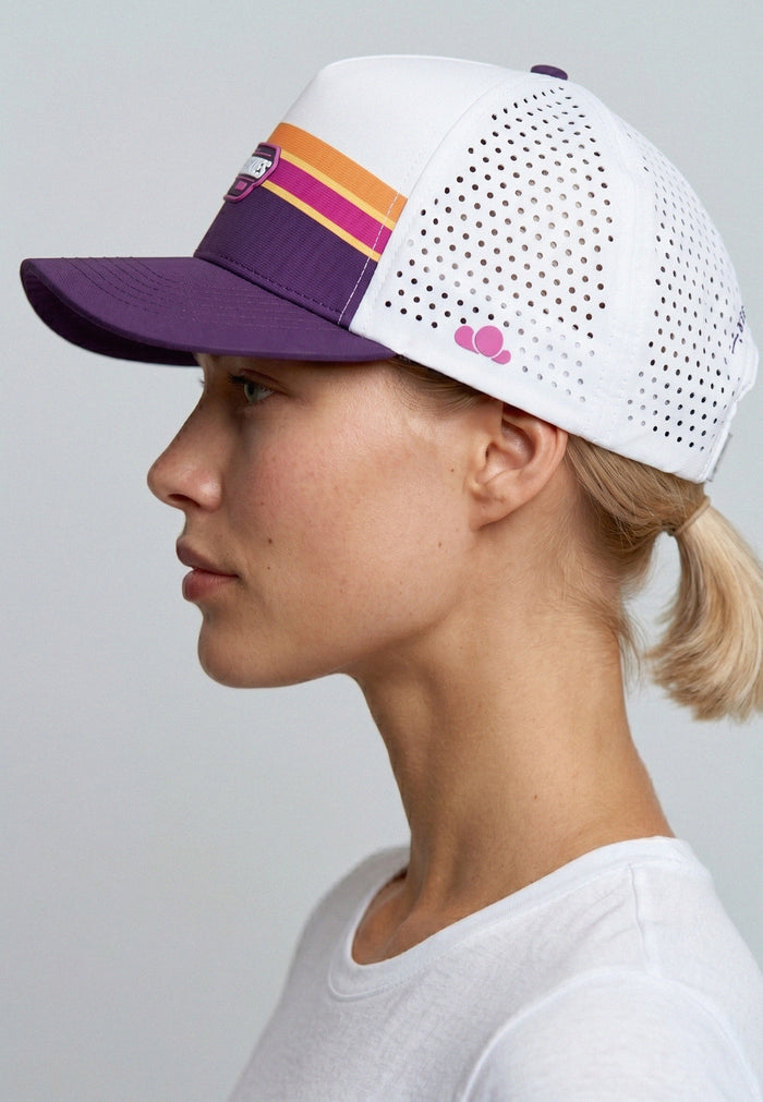 Person wearing a white and purple cap with pink heart design on a gray background