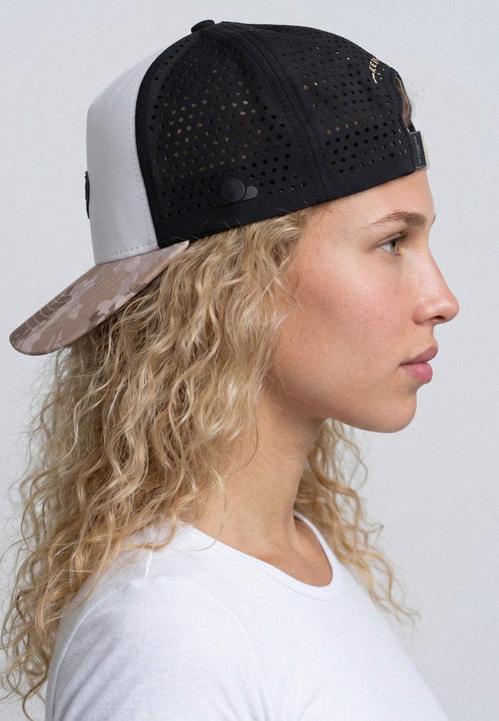 Woman wearing a black and white cap with a camouflage bill against a plain background