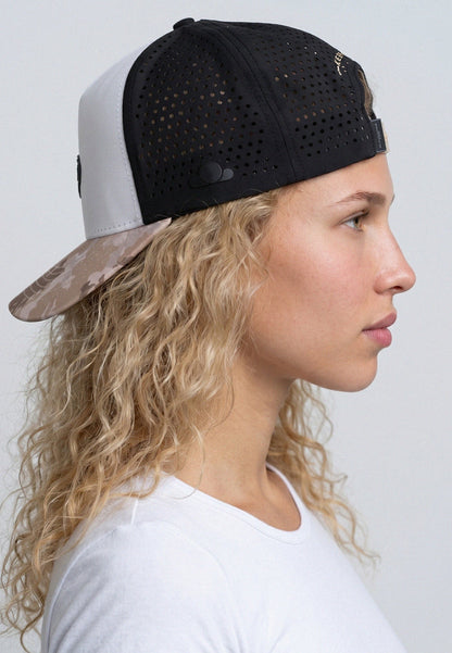 Woman wearing a black and white cap with a camouflage bill against a plain background
