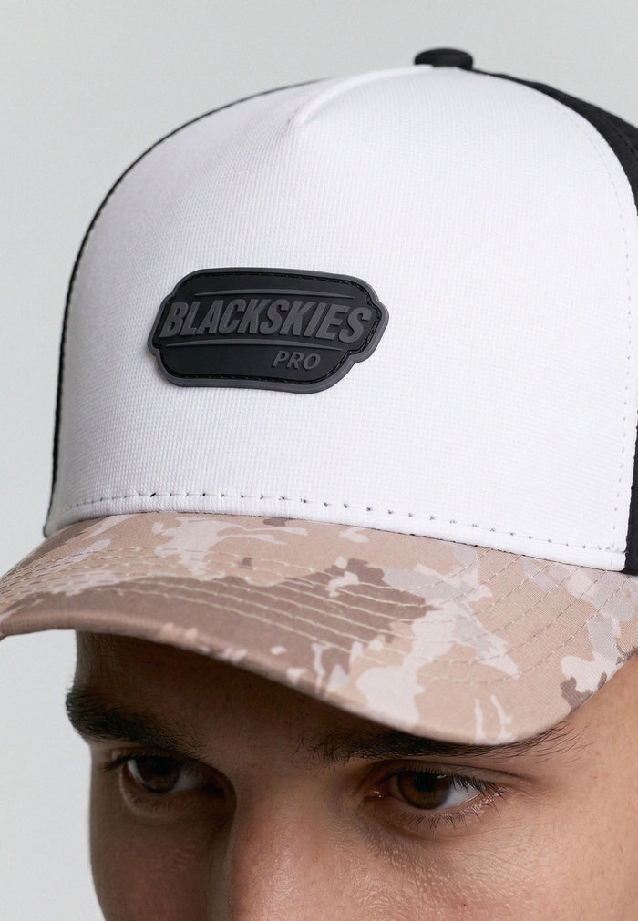 White cap with camouflage brim and 'BLACKSKIES' logo on a plain background
