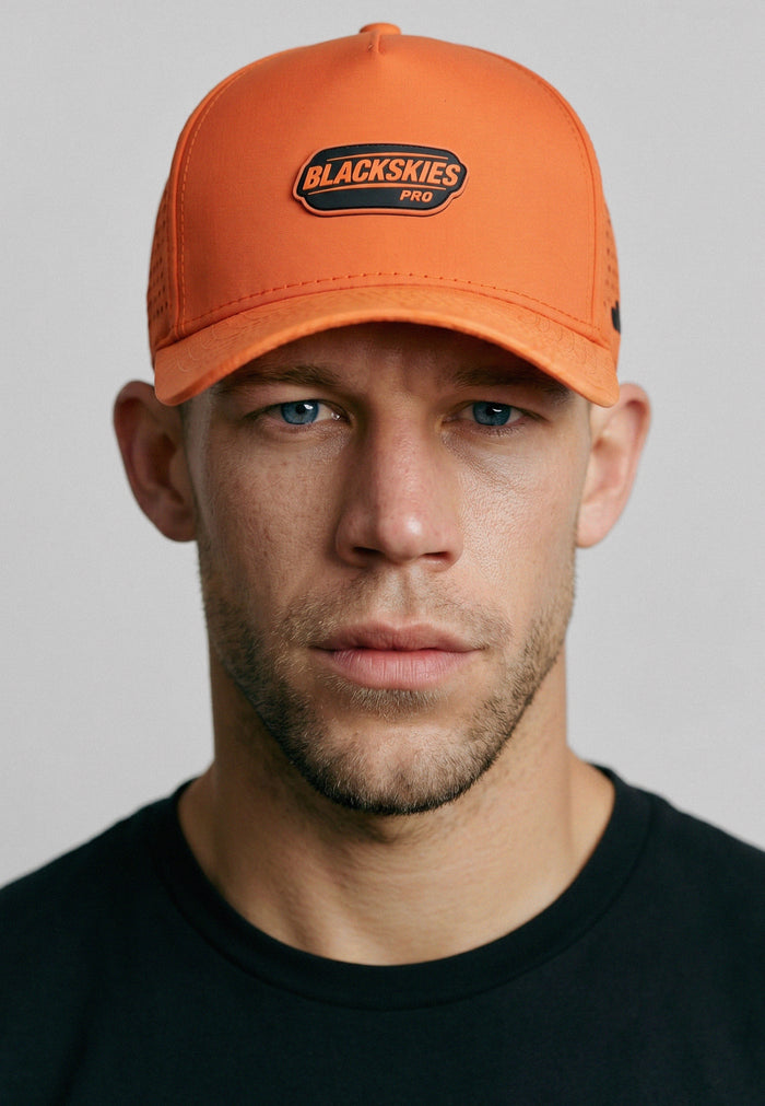 Man wearing an orange cap with 'Blackskies Pro' logo on a gray background