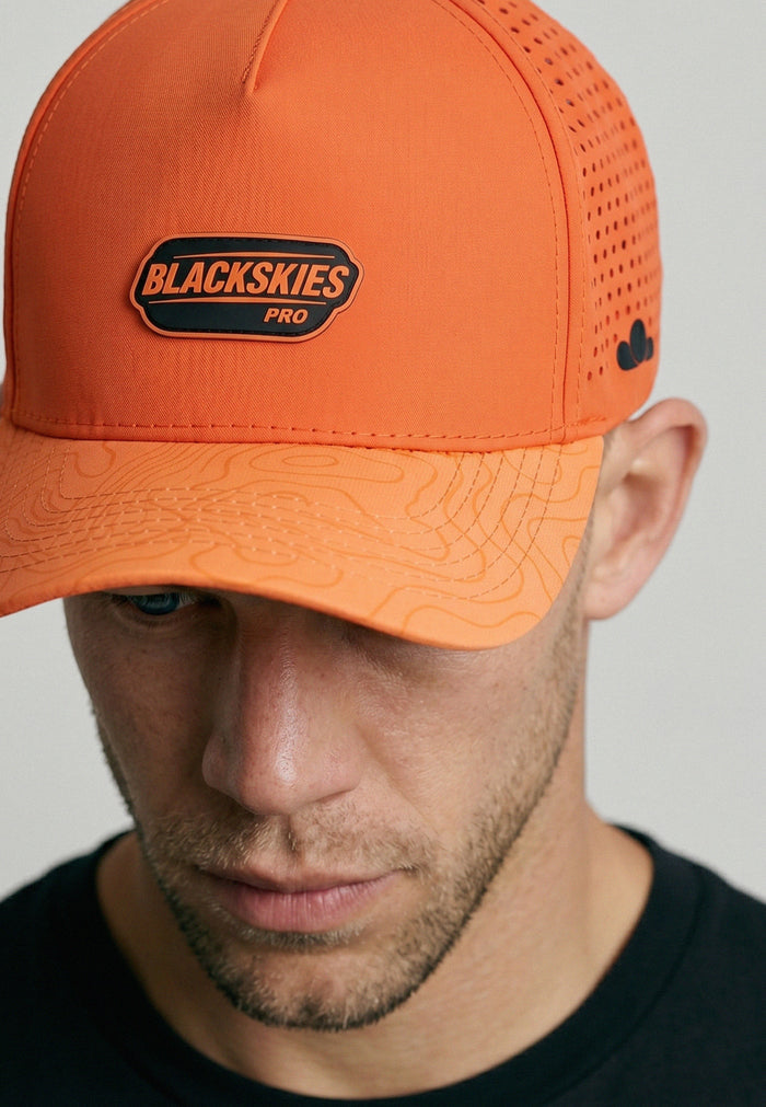Man wearing an orange cap with 'Blackskies Pro' logo on a plain background