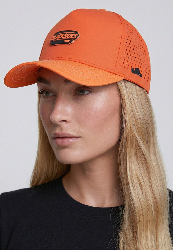 Person wearing an orange cap with a brand logo on a plain background
