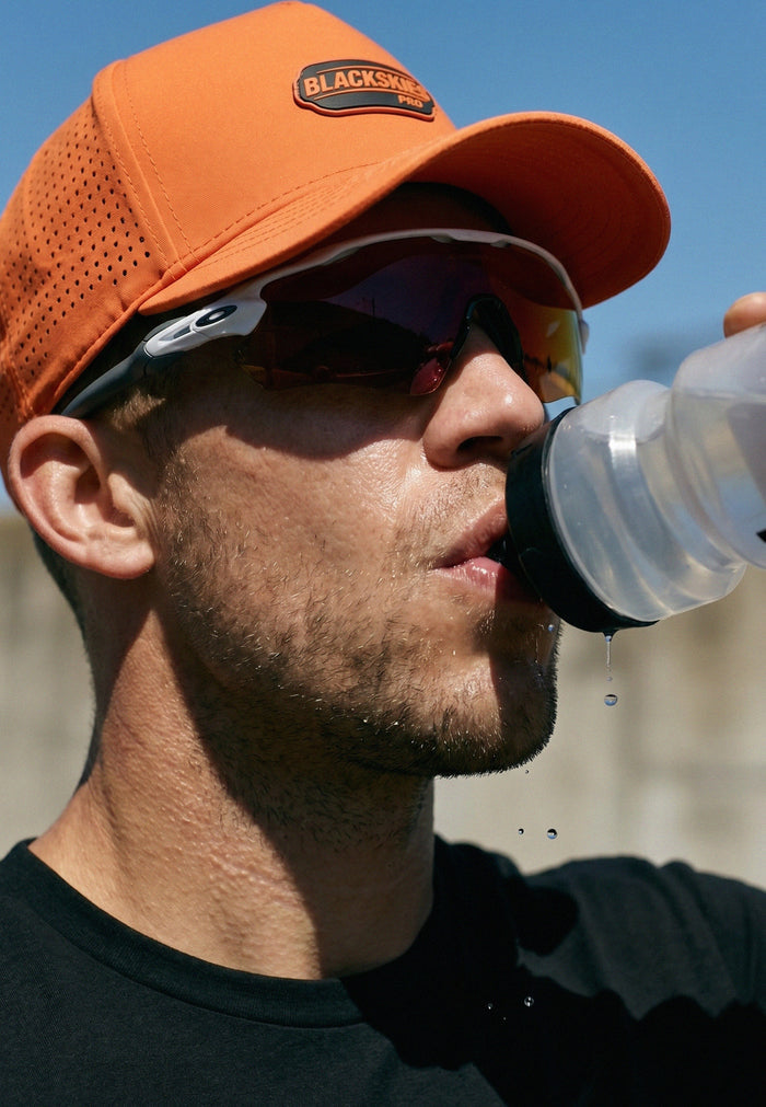 Man wearing an orange cap with a Blackstone Pro logo, drinking from a water bottle.