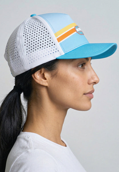 Woman wearing a white and blue cap with colorful accents on a gray background