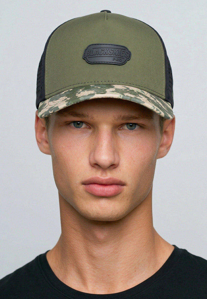 Man wearing a green and camouflage cap with a black patch on a gray background