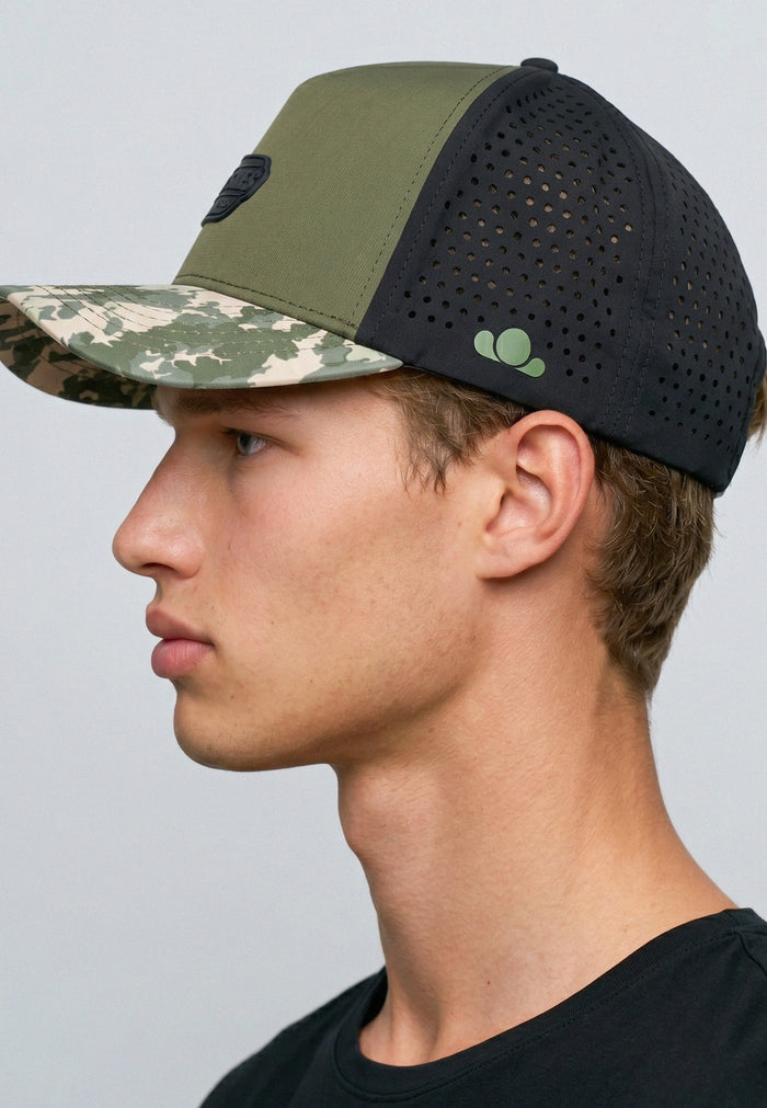 Person wearing a cap with camouflage and black design on a plain background